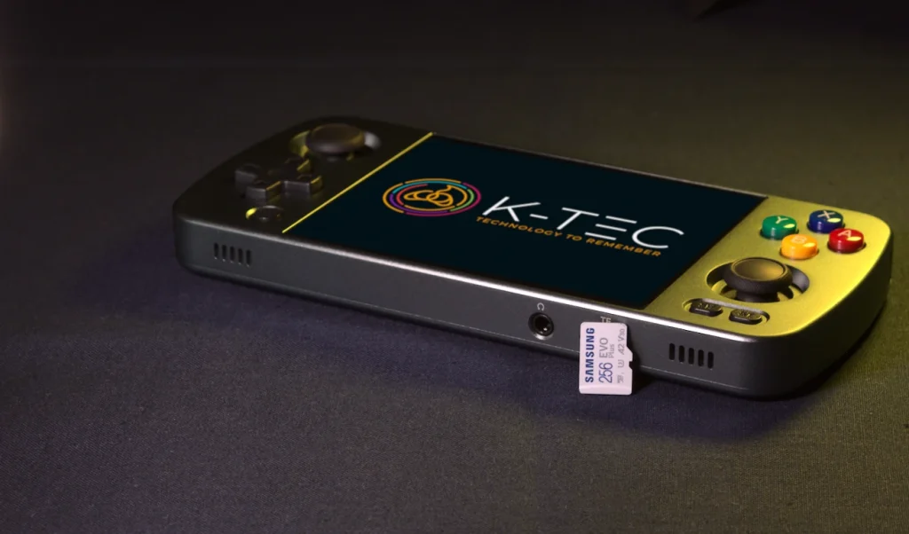 A genuine Samsung MicroSD card leaning against a grey metal retro gaming handheld on navy fabric, lit with a gold rim light.